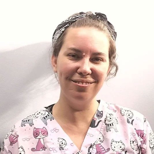 smiling female veterinary assistant standing in front of white wall